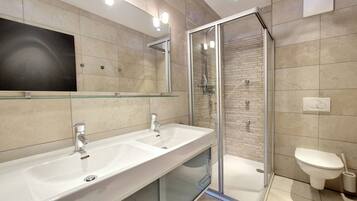 A modern bathroom with a glass-enclosed shower, two sinks, and a toilet.