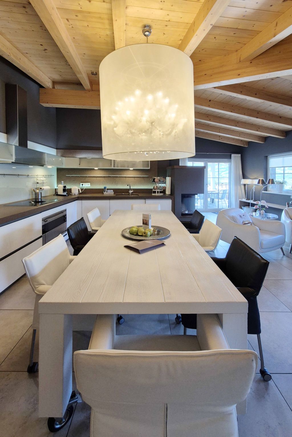 A modern kitchen with a large dining table, white chairs, and a hanging light fixture.