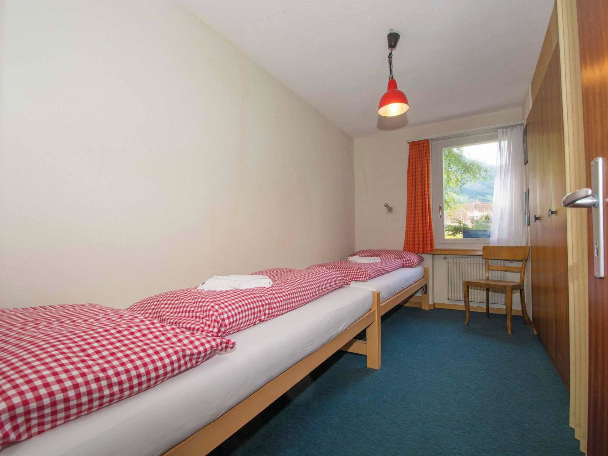 A single-bed room with a wooden bed, a desk, and a window with curtains.