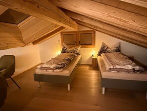 Ein gemütliches Schlafzimmer im Dachgeschoss mit zwei Betten, Holzbalken und einer geneigten Decke.