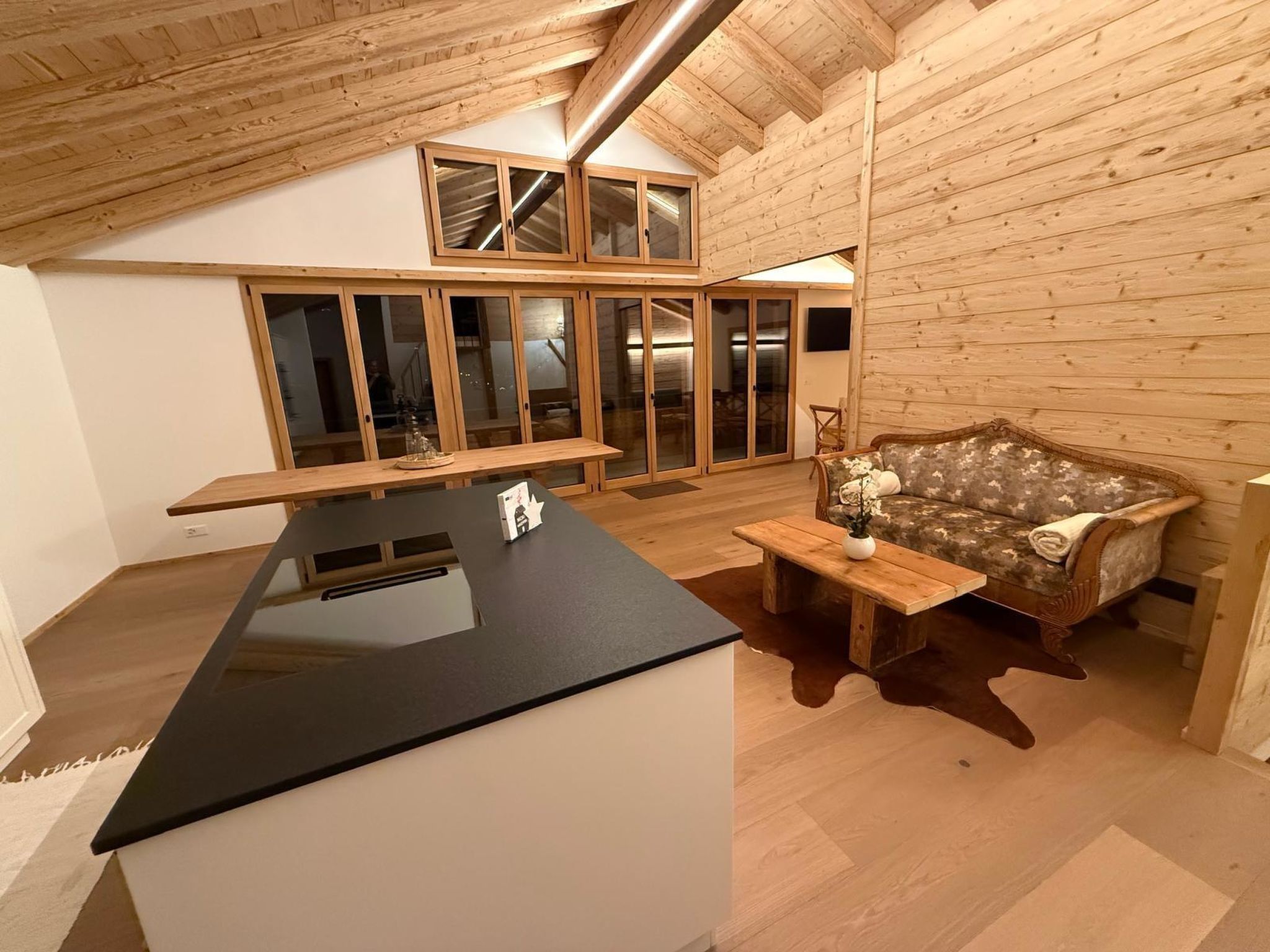 A modern kitchen with a black countertop, wooden cabinets, and a dining area with a sofa and bench.