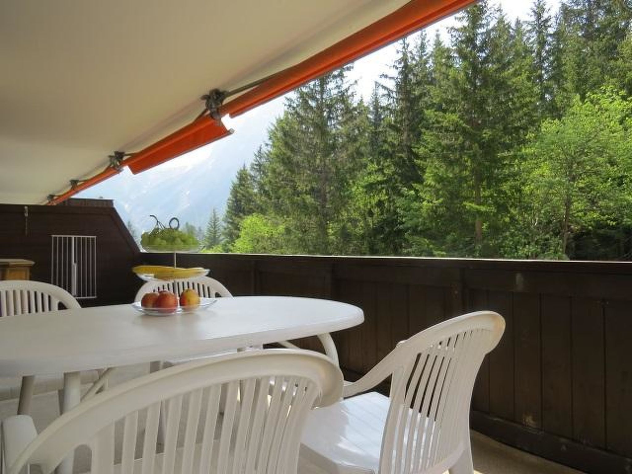 Eine Terrasse im Freien mit Tisch und Stühlen, ein Holzdeck und Blick auf einen bewaldeten Bereich.