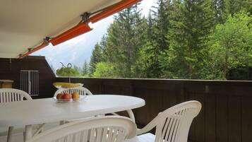 Eine Terrasse im Freien mit Tisch und Stühlen, ein Holzdeck und Blick auf einen bewaldeten Bereich.