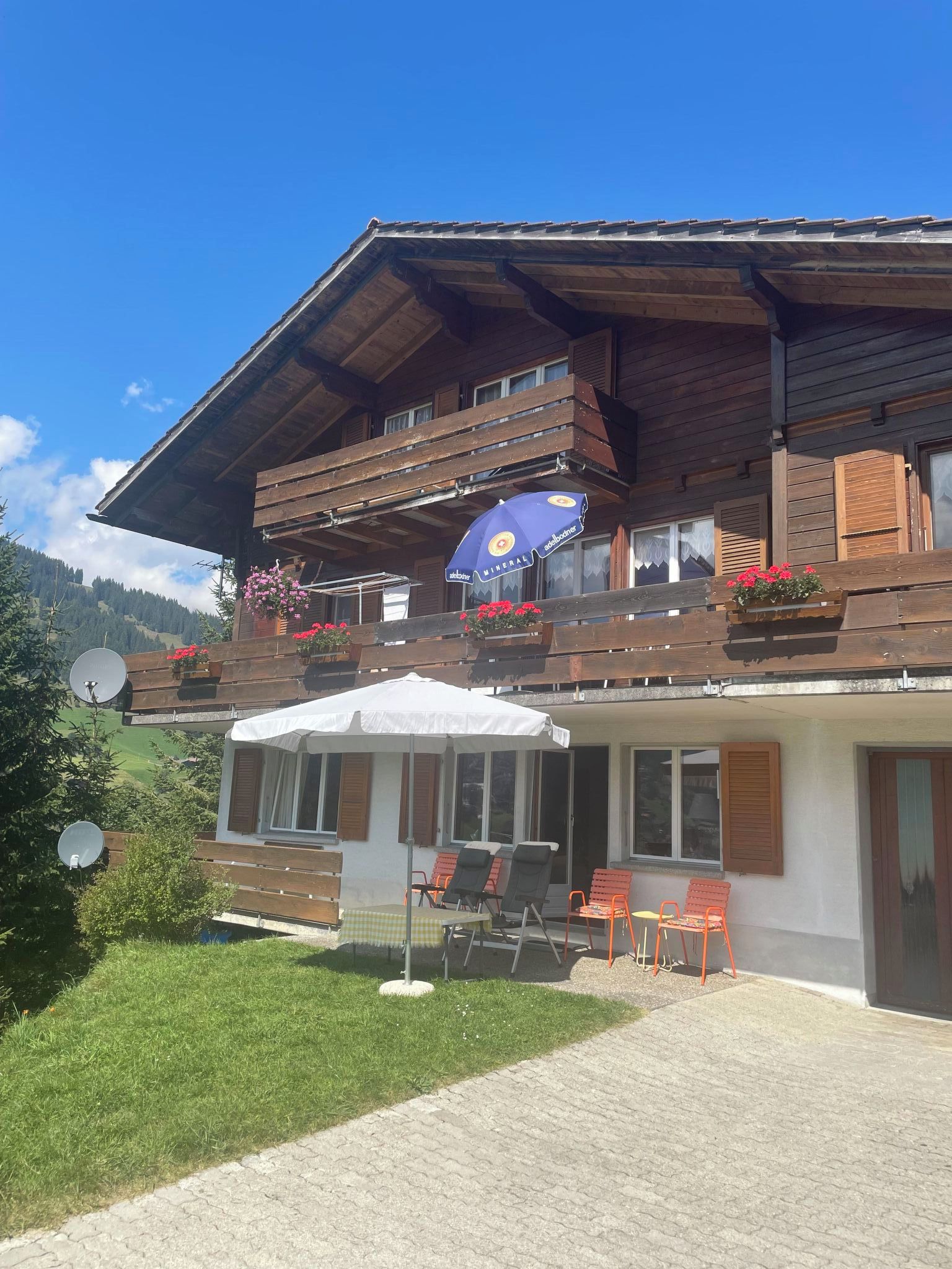 A two-story wooden building with a balcony, outdoor seating, and a view of a mountainous landscape.