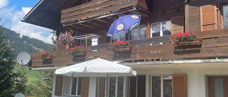 Un bâtiment en bois à deux étages, doté d’un balcon, d’un espace extérieur aménagé pour s’asseoir et offrant une vue sur un paysage montagneux.