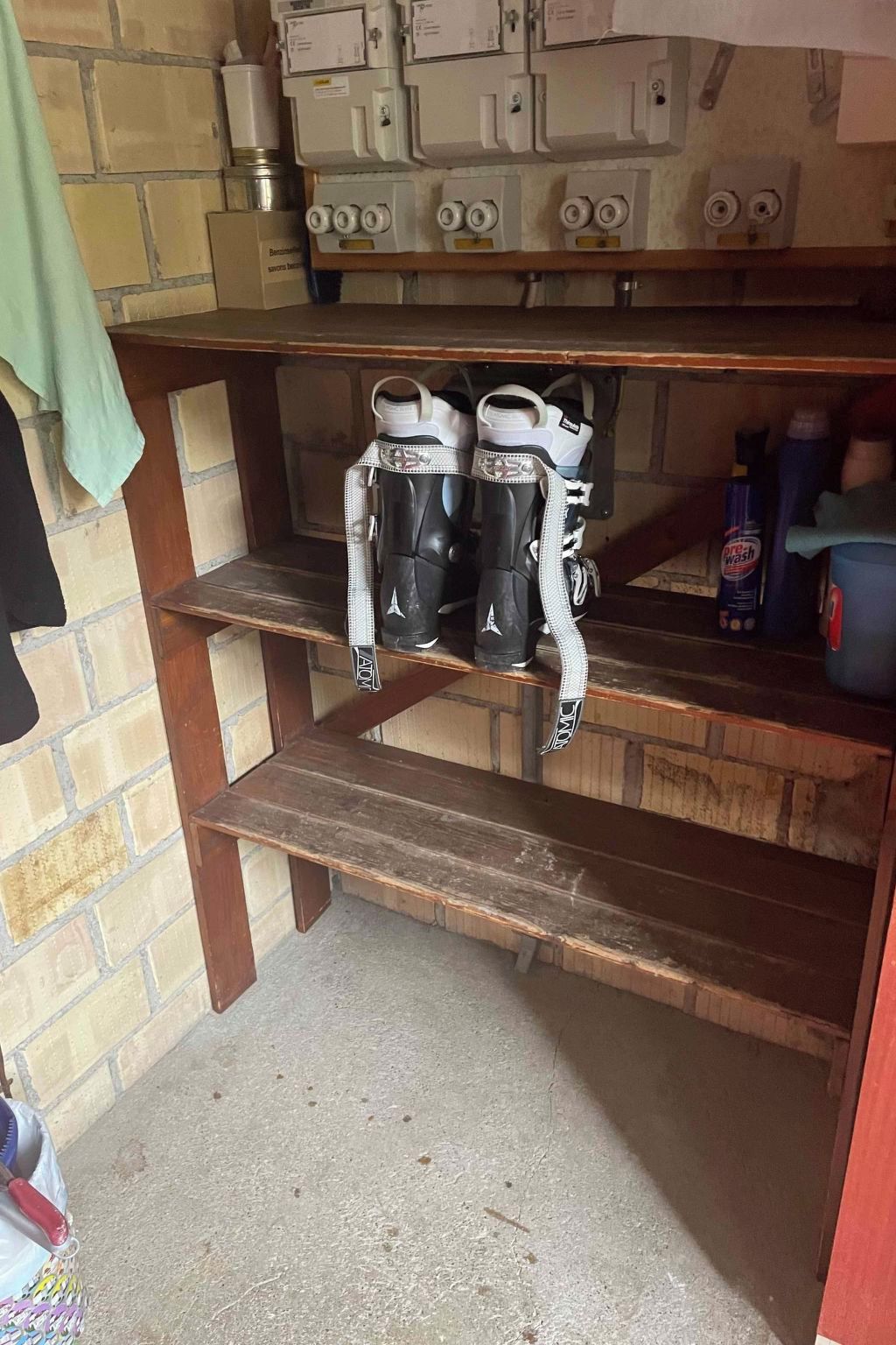 A room with a brick wall, a shelf with boots, and a shelf with cleaning supplies.
