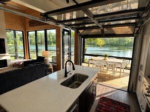 Une cuisine moderne dotée d’un grand îlot central, d’un coin repas offrant une vue sur un lac et d’un espace salon confortable avec une cheminée.