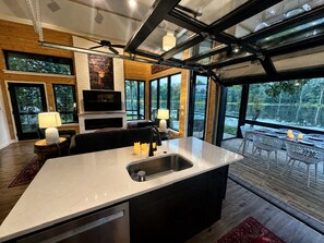 Une cuisine moderne dotée d’un grand îlot central, d’appareils électroménagers intégrés et offrant une vue sur une terrasse avec coin salon extérieur.