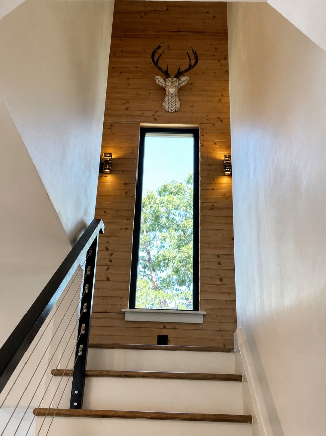 Eine Treppe mit Holzwertlauf und Blick auf Bäume durch ein Fenster.