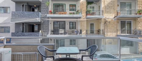 Un balcón con una mesa y sillas, con vistas a una calle con coches estacionados y edificios.