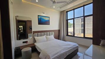 A hotel room with a bed, a bedside table, a mirror, a window with a view of the outside, and a ceiling fan.