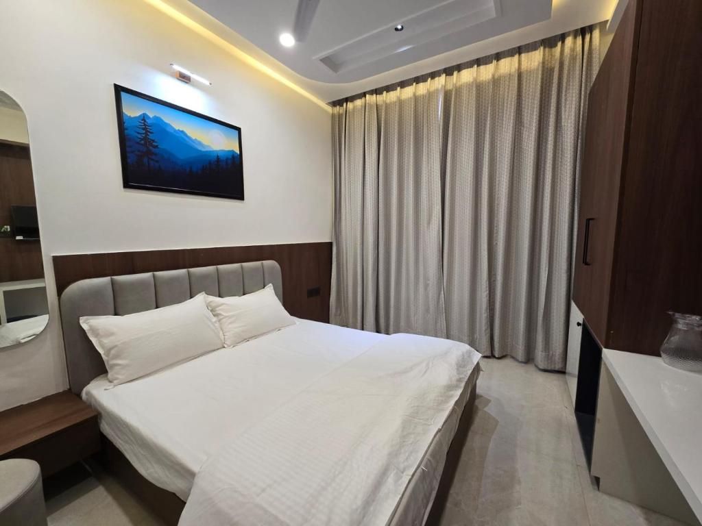 Habitación de hotel con cama, mesita de noche, espejo, un cuadro en la pared y ventana con cortinas.