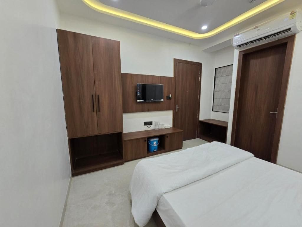 A bedroom with a bed, a TV mounted on a wooden cabinet, a small shelf, and a door with a window.