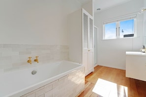Een moderne badkamer met een wit ligbad, twee gouden kraanwerk en een wand betegeld met witte tegels.