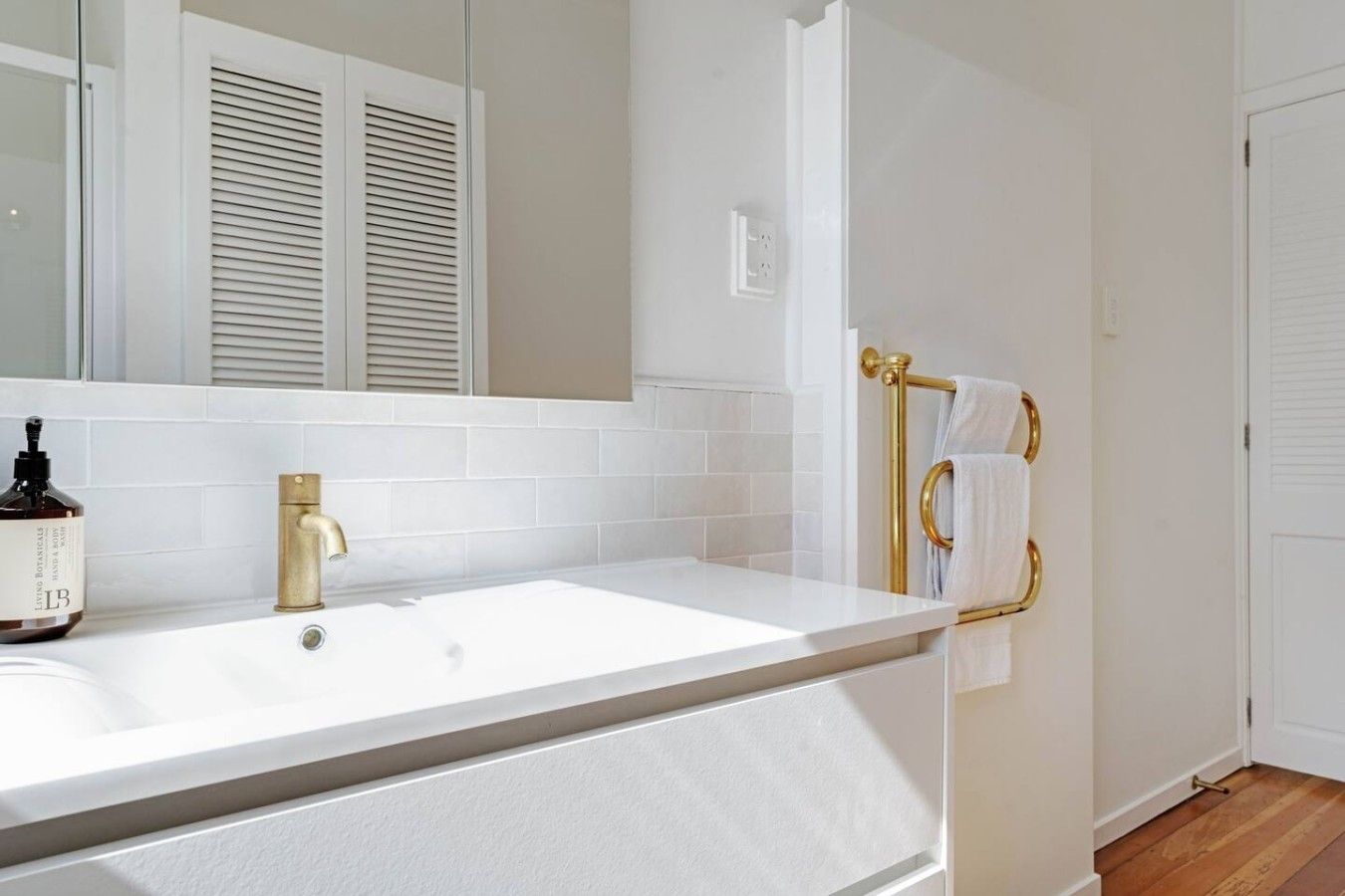 A bathroom with a white sink, gold faucet, and towel rack.