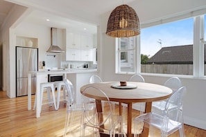 Een moderne keuken met witte kasten, een ronde houten eettafel en transparante plastic stoelen.