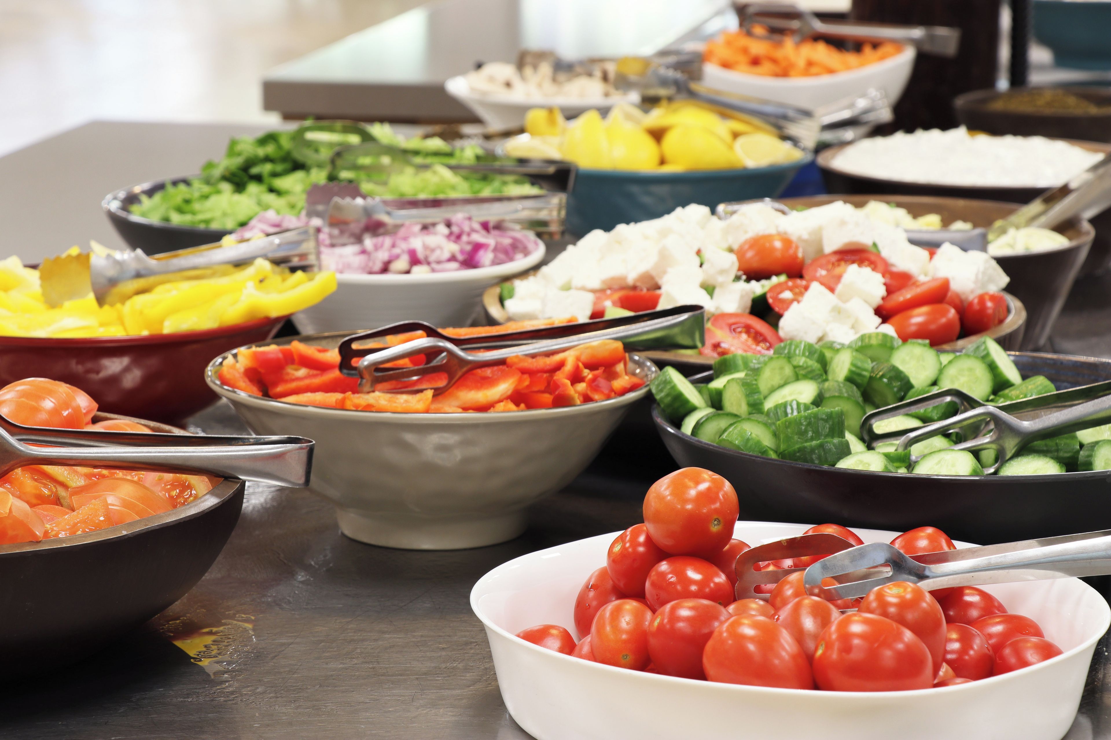 A buffet table with various food items including tomatoes, cucumbers, and other vegetables.