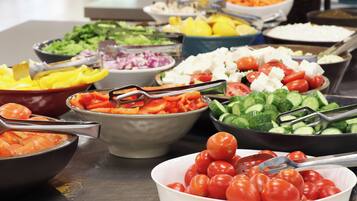 A buffet table with various food items including tomatoes, cucumbers, and other vegetables.