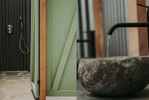A bathroom with a shower, a green door, and a stone basin with running water.