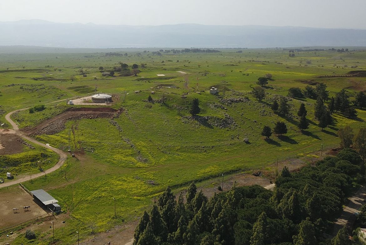Paisaje rural con una construcción circular, posiblemente un granero o almacén, rodeado de campos y árboles.