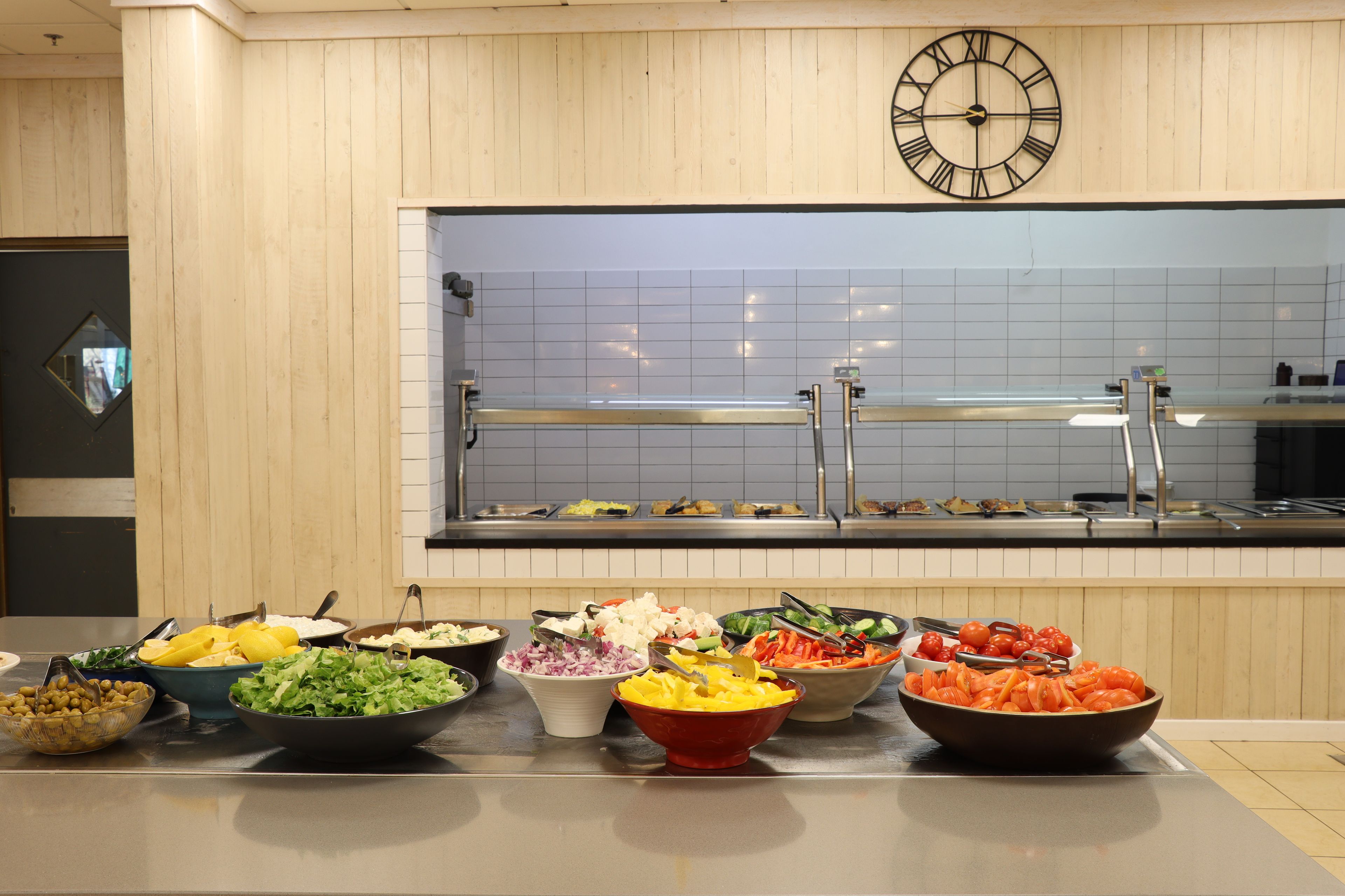 A buffet area with various food options and a clock on the wall.
