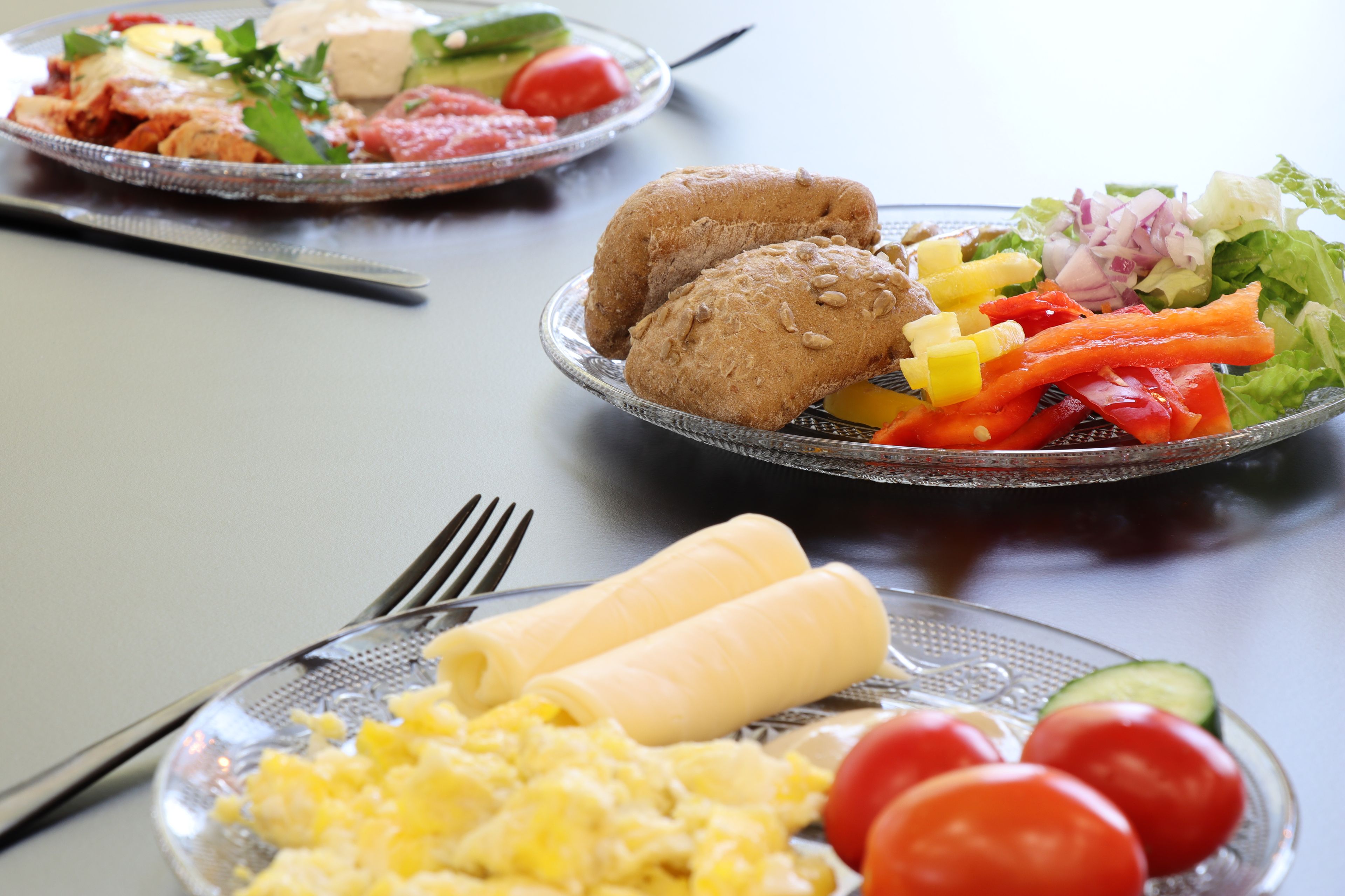 A dining table with plates of food, including vegetables, eggs, and bread.