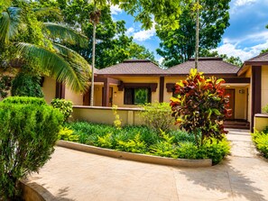 Un edificio residencial con entrada de baldosas, rodeado de jardines cuidados y palmeras.