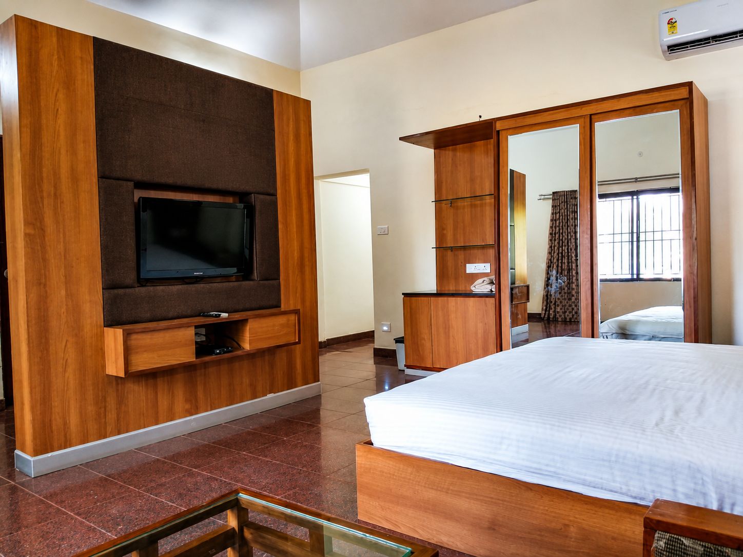 Una habitación de hotel moderna con una cama grande, un televisor montado en un panel de madera, un armario y un espejo.