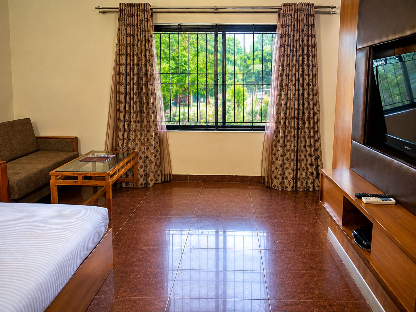 A hotel room with a bed, a sofa, a small table, a TV, and a window with curtains.
