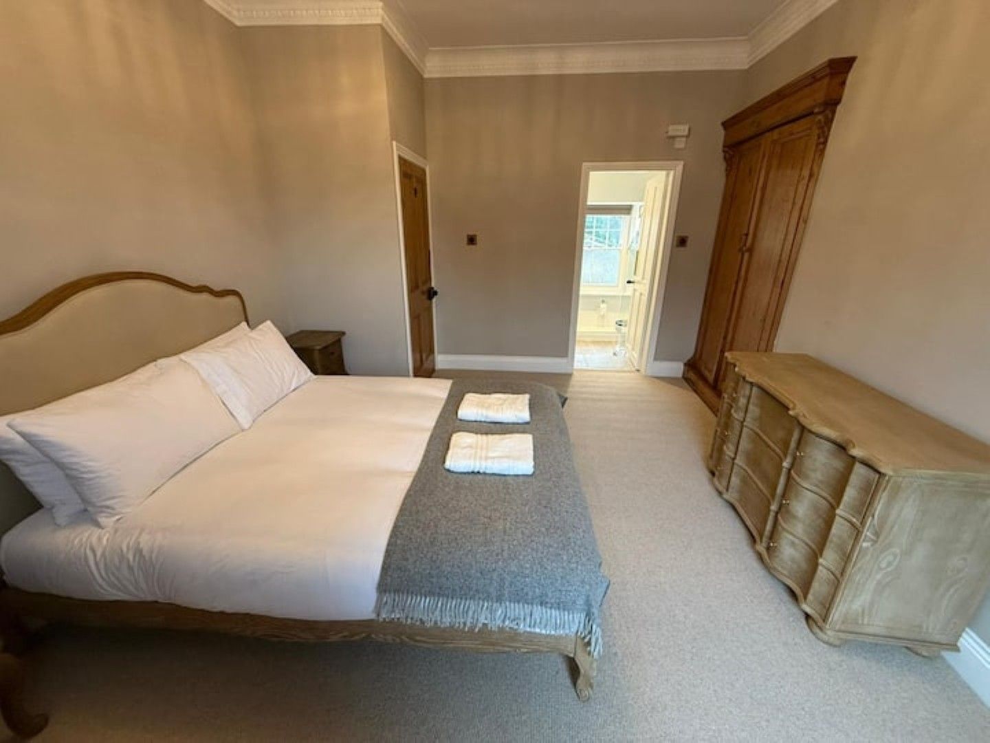 Une chambre à coucher avec un grand lit, une table de chevet, une armoire et une porte donnant sur une salle de bain.