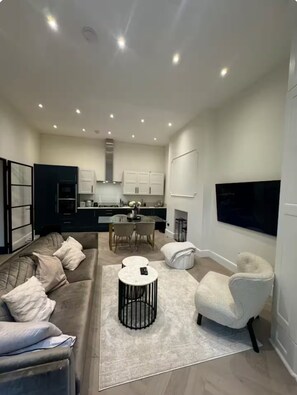 Een moderne woonkamer met een bank, fauteuils, een salontafel en een aan de muur bevestigde televisie.