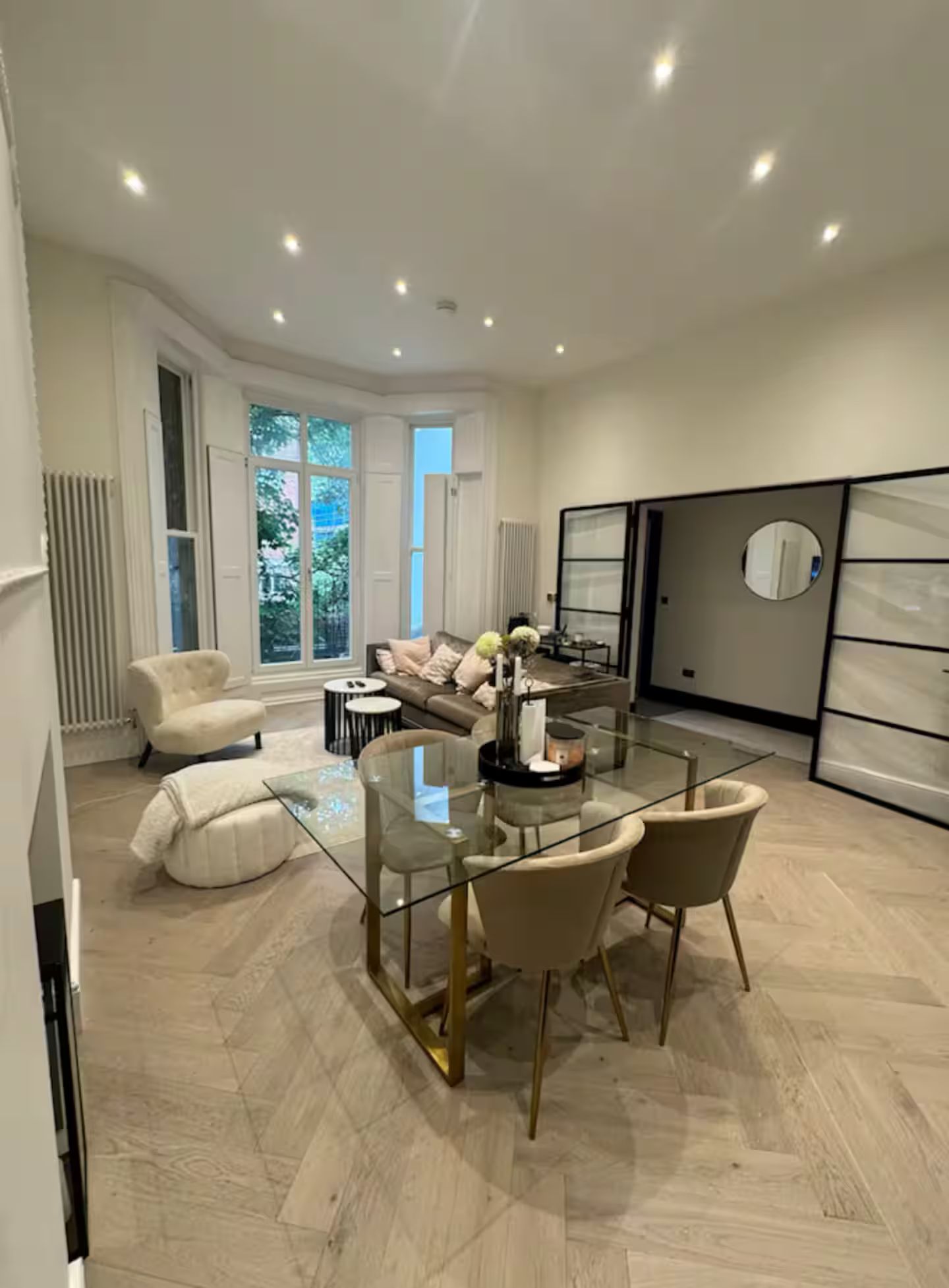 Un salon moderne avec une table à manger en verre, des canapés de couleur beige et une grande fenêtre.