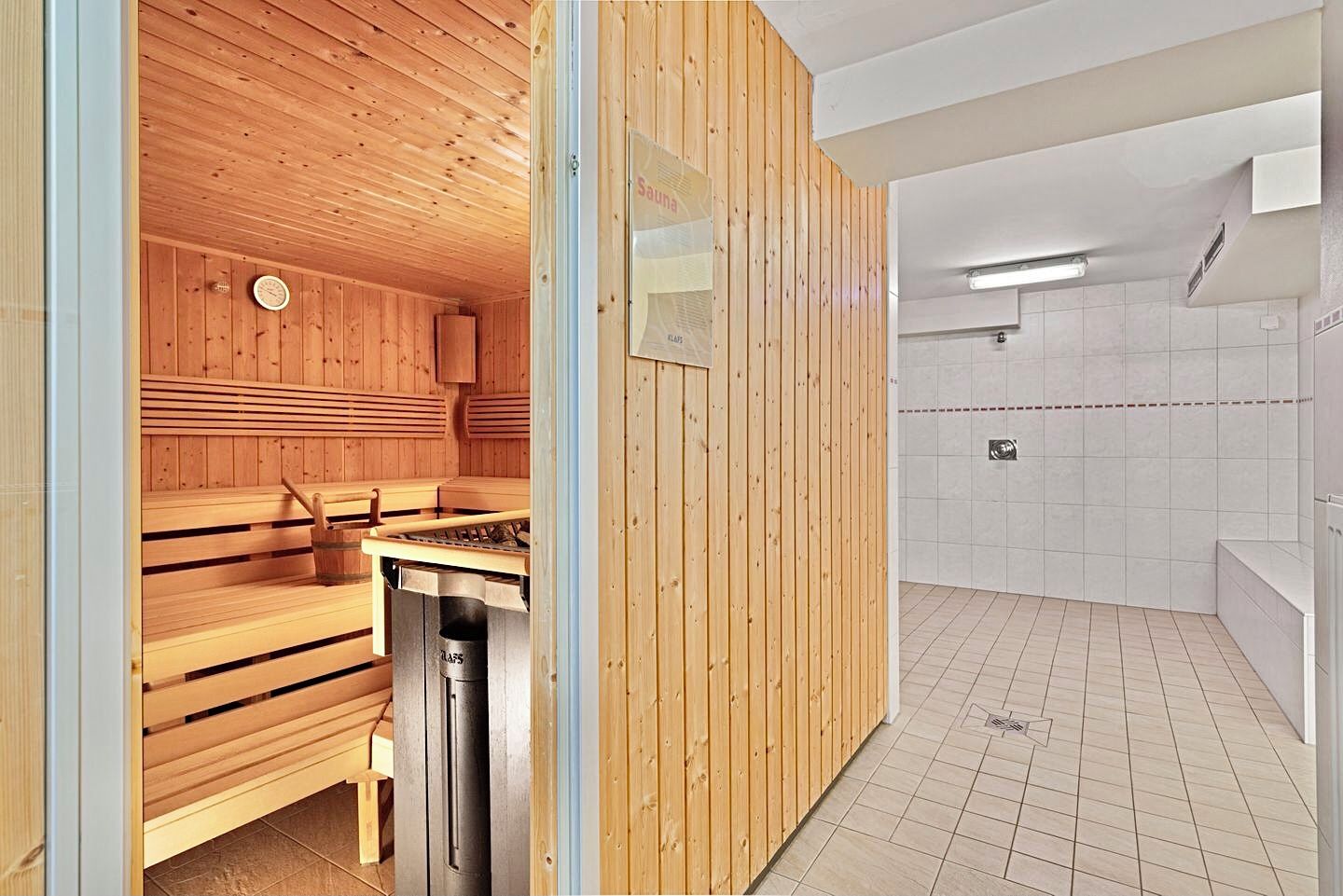 Una sauna con bancos de madera y una zona de ducha de vapor con paredes de azulejos y un banco.