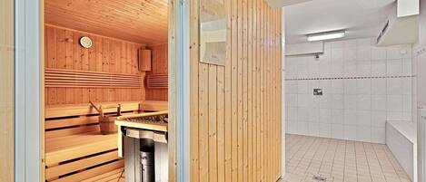Una sauna con bancos de madera y una zona de ducha de vapor con paredes de azulejos y un banco.