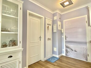 A hallway with a cabinet, a door with a nameplate, a wall-mounted phone, and a door with a beach scene. - Ostseestrand-23, prime beachfront location, balcony, elevator, sauna (Kühlungsborn)
