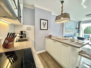 A modern kitchen with white cabinets, a built-in stove, and a hanging light fixture. - Ostseestrand-23, prime beachfront location, balcony, elevator, sauna (Kühlungsborn)