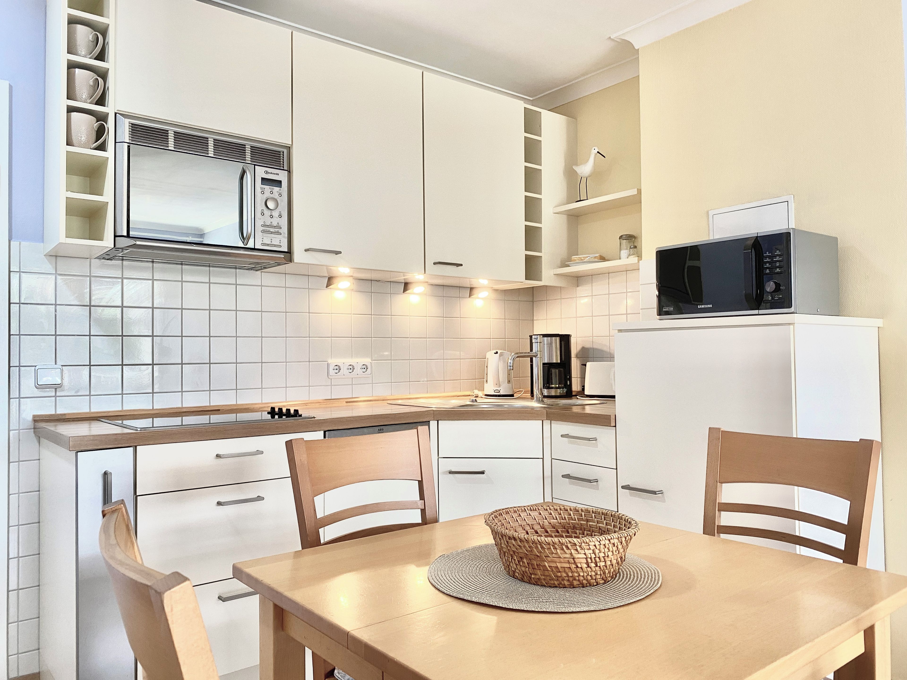 Una cocina moderna con armarios blancos, microondas, cafetera y una mesa de comedor con sillas.