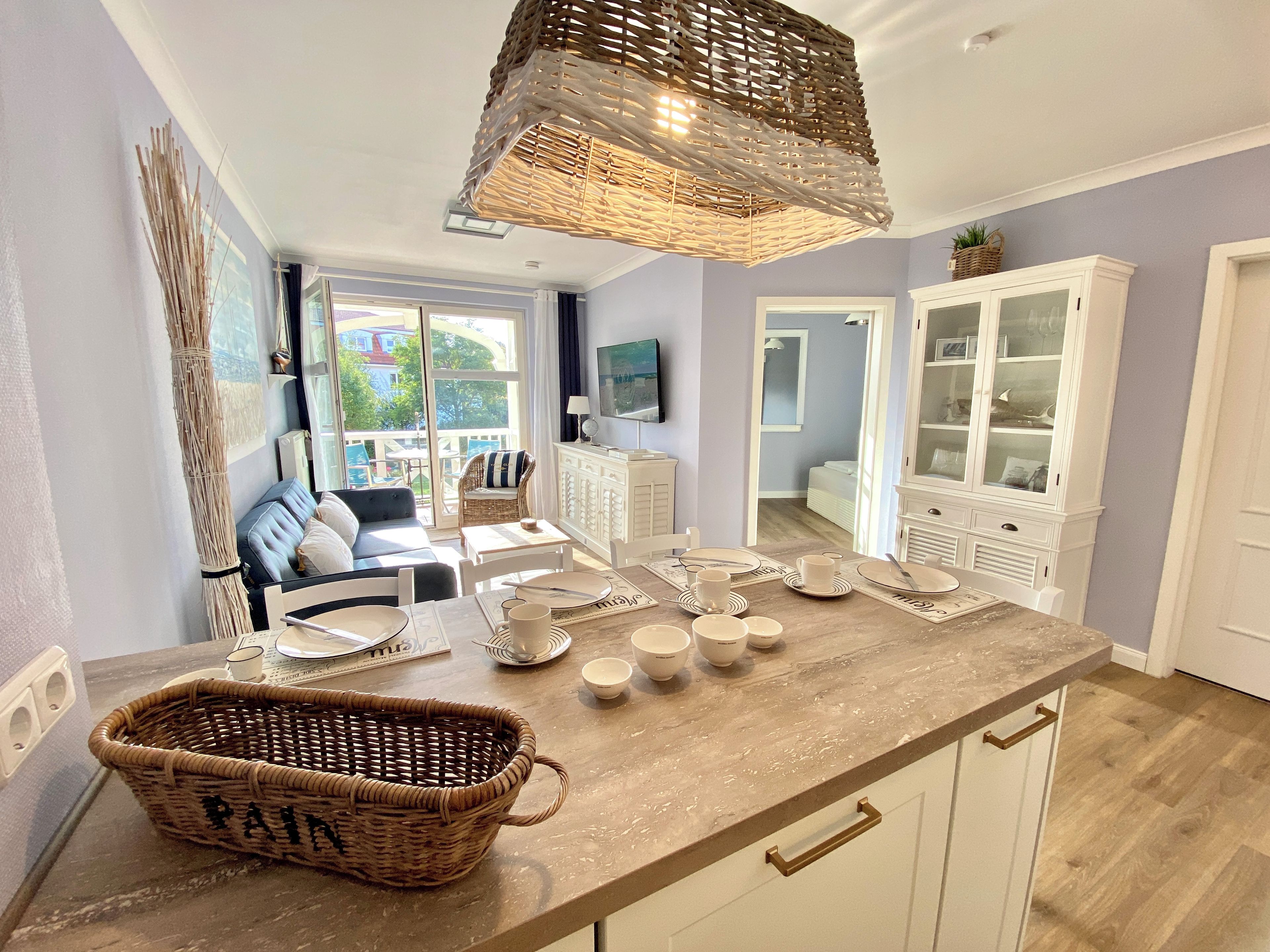 Cocina bien iluminada con una isla central, muebles de cocina blancos y una cesta de mimbre en la encimera.