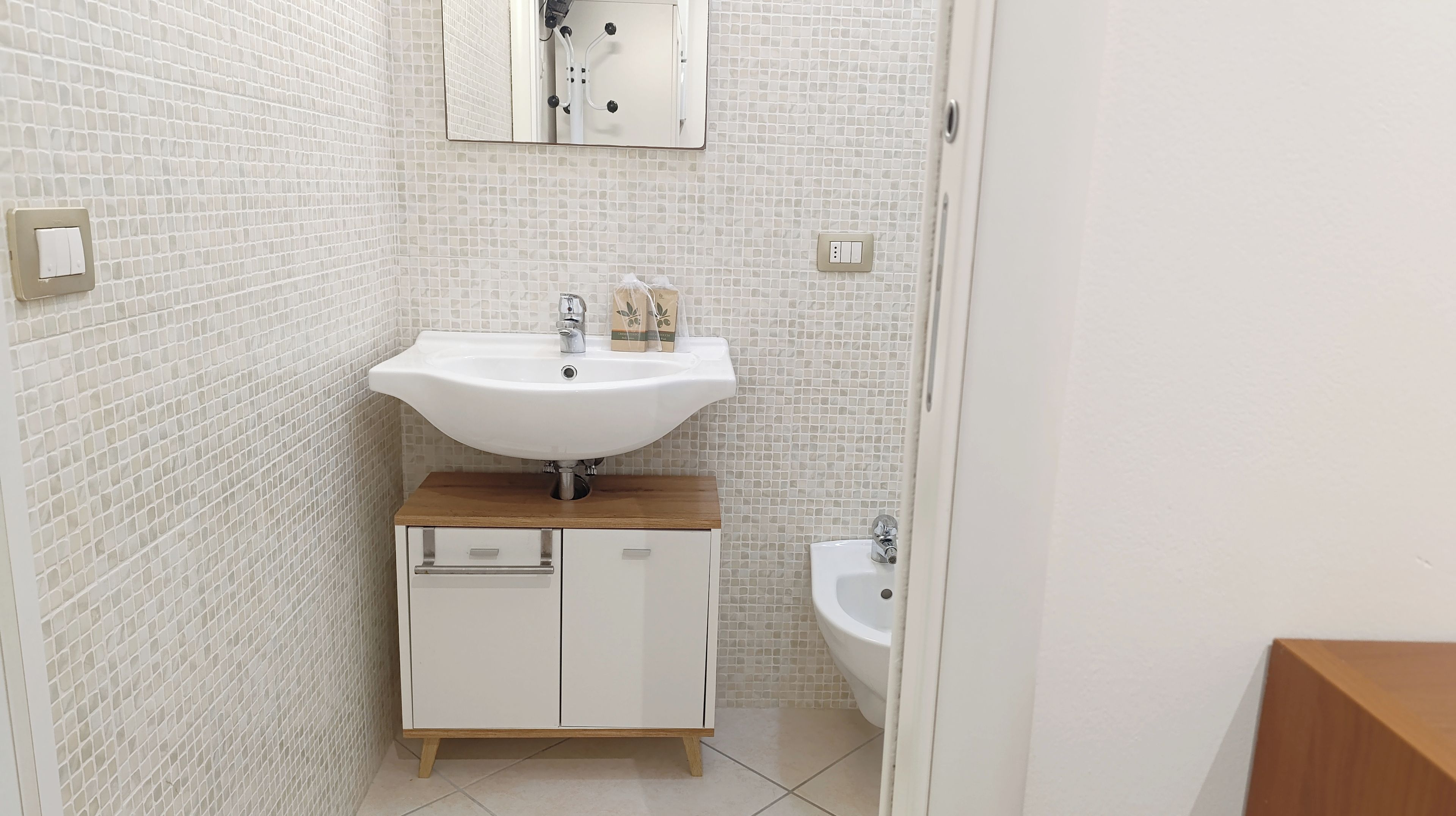 A bathroom with a white sink, wooden countertop, and a mirror above it.