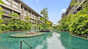 A swimming pool with lounge chairs and a hot tub, surrounded by lush greenery and modern buildings. - Naya by Kozystay - Nusa Dua (Kuta)