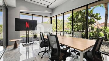 A modern conference room with a large table, black office chairs, and a TV screen displaying the Netflix logo.