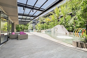 A modern indoor pool area with a glass ceiling, lounge seating, and a mural wall. - Naya by Kozystay - Nusa Dua (Kuta)