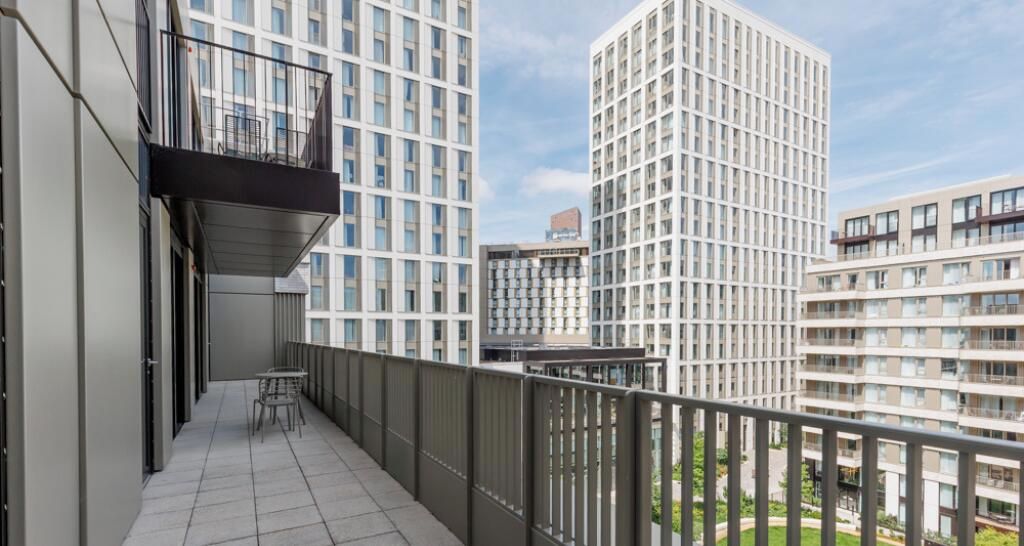 Ein Balkon mit Blick auf hohe Gebäude, einem Geländer und einem Tisch mit Stühlen.