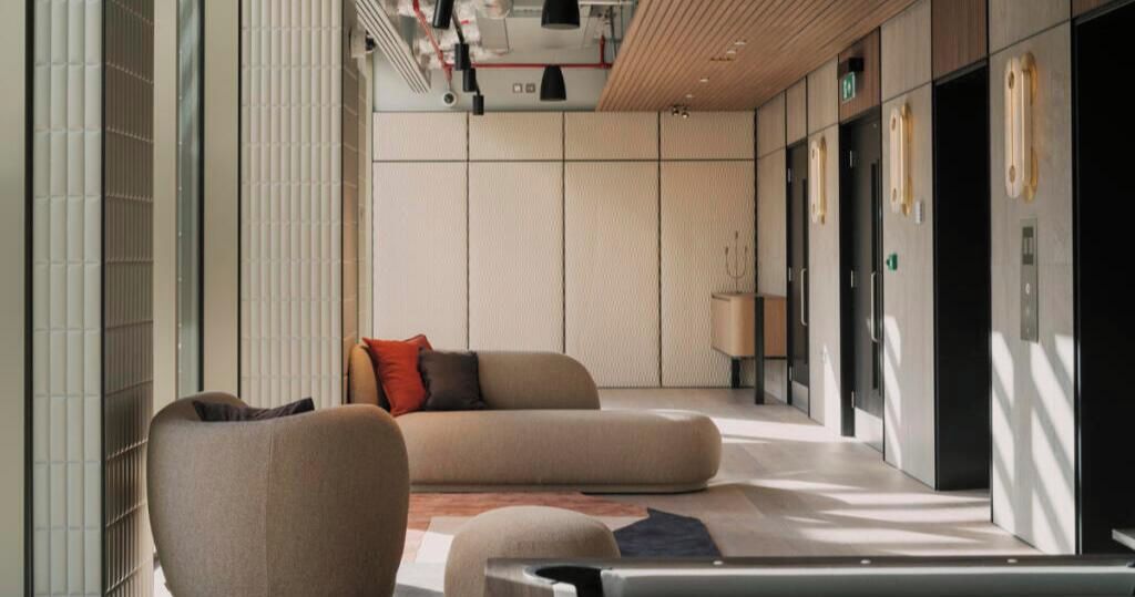 A modern lobby with a sofa, a chair, and a lamp.