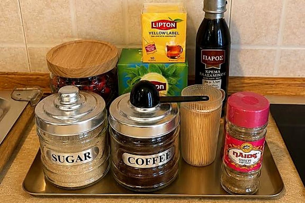 Un piano di lavoro in cucina con un contenitore di zucchero, uno di caffè, una scatola di tè Lipton, una bottiglia d'olio d'oliva e un barattolo di spezie.