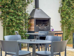 Eine Terrasse im Freien mit einem Grill, einem runden Tisch und vier Stühlen.