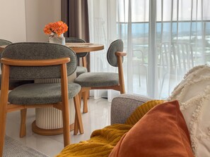 Ein modernes Wohnzimmer mit Essbereich, ausgestattet mit einem runden Tisch, grauen Polsterstühlen und Blick durch große Fenster.