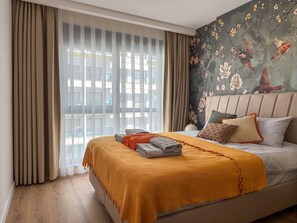 Ein Hotelzimmer mit einem großen Bett, einem Fenster mit Vorhängen und einer Wand mit einer floralen Wandmalerei.