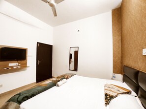 A hotel room with a bed, a television mounted on the wall, a door, and a mirror. - Premium Rooms For Corporates, Couples, Families, Students And Travelers (Ludhiana)