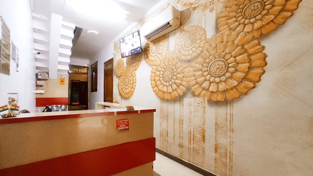 A hotel reception area with a red and beige striped counter, a wall-mounted air conditioning unit, and a floral-patterned wall. - Premium Rooms For Corporates, Couples, Families, Students And Travelers (Ludhiana)
